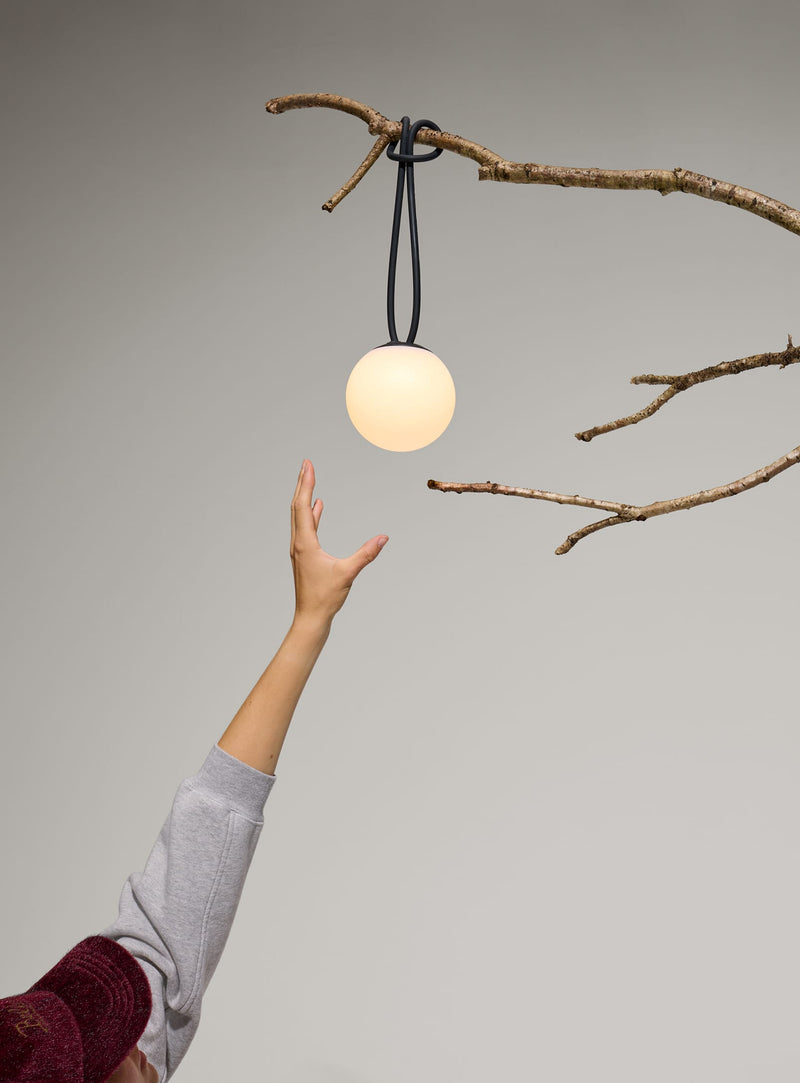 Lampe Bolleke la Surprise rouge suspendue à une branche d’arbre pour une soirée en plein air.